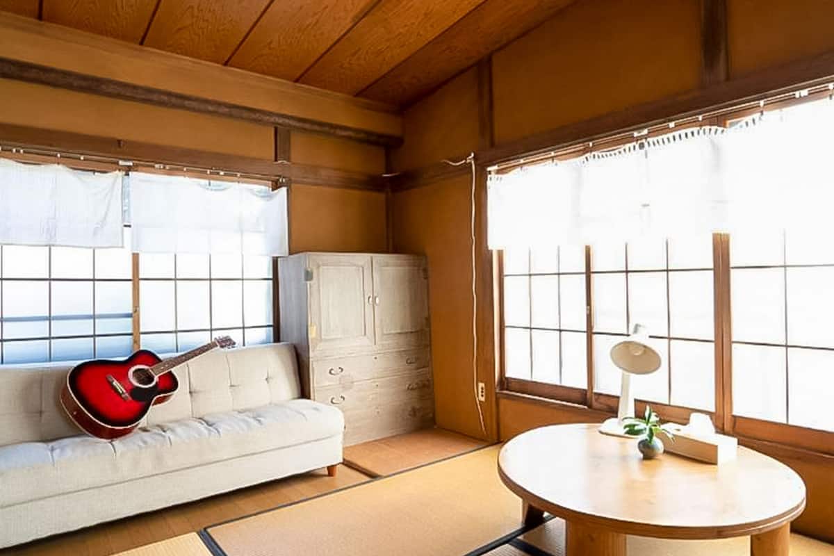 Perinteinen japanilainen huone, jossa on tatamimatto, matala puupöytä, kitaraa koristeleva sohva ja liukuvat ovet.