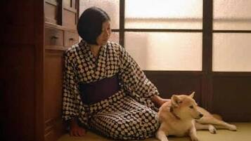 Una persona sentada sobre un suelo de tatami junto a una ventana, con un perro acostado a su lado.