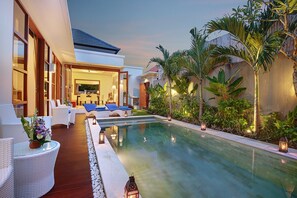A poolside area with lounge chairs and a dining area, surrounded by tropical plants and a modern building. - Lucia Villa Seminyak (Seminyak)