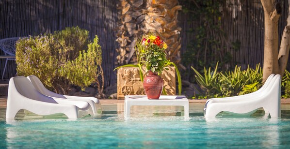 Una piscina al aire libre, sombrillas, sillones reclinables de piscina