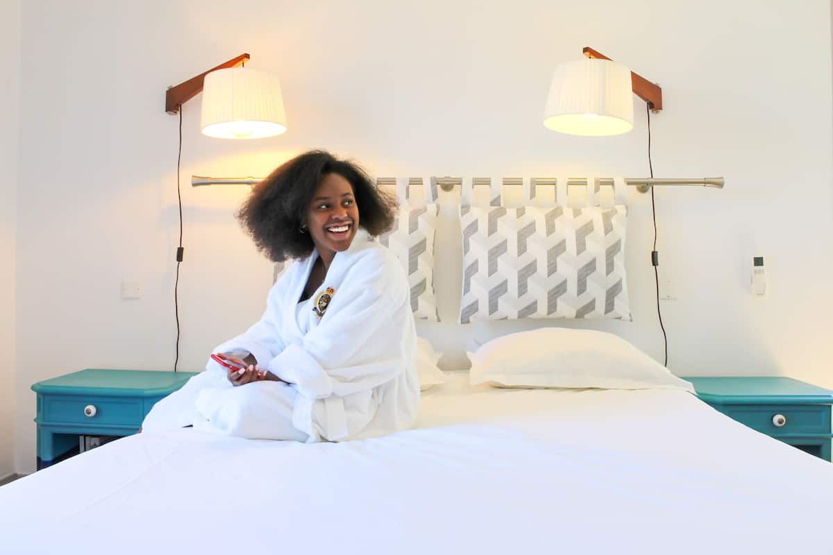 A bed with a white headboard, two bedside tables, and a wall-mounted lamp.