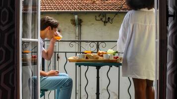 A balcony with a tiled roof, a table with food, and a person sitting and another standing.