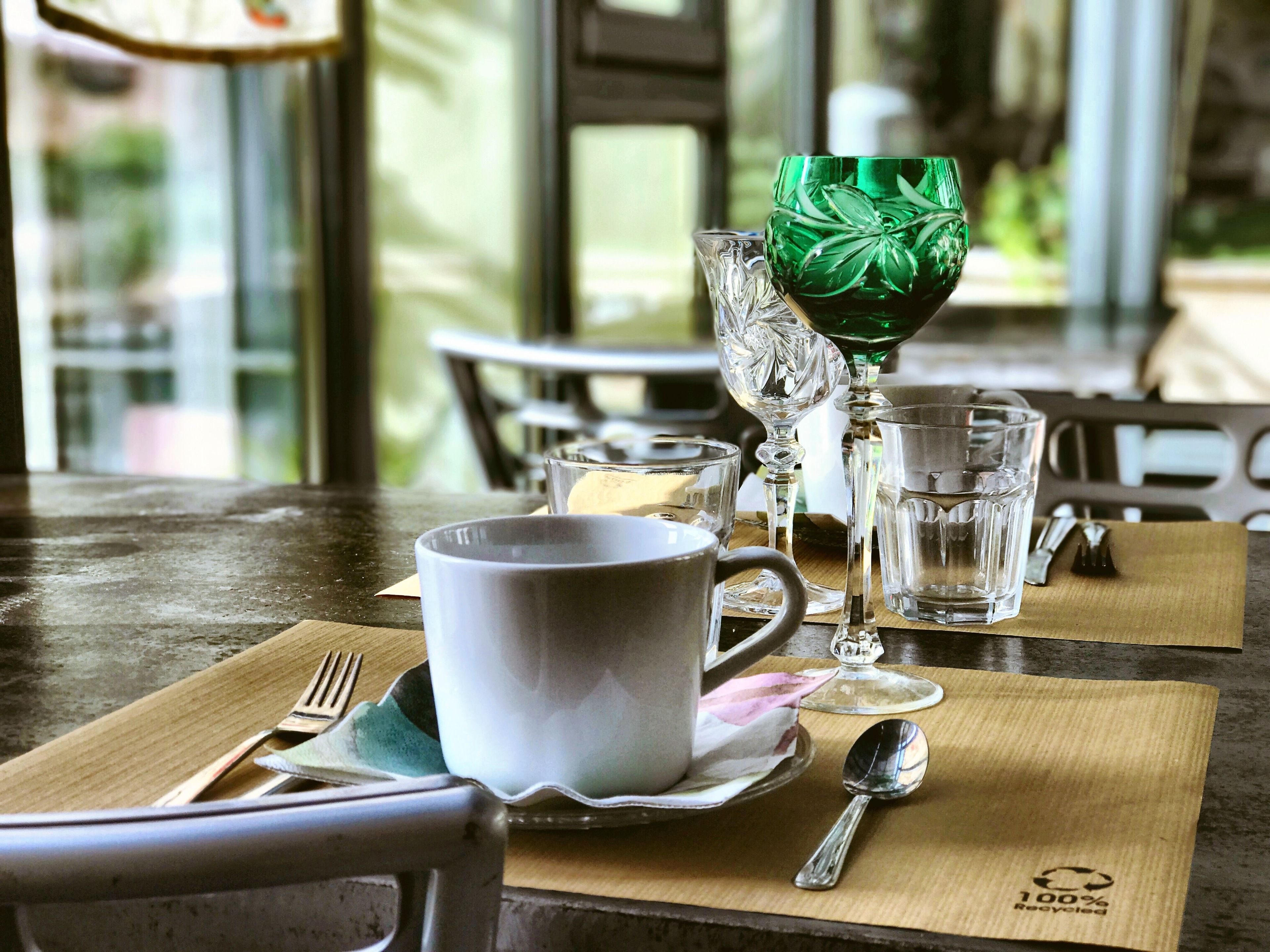 A dining table with a white mug, a green glass, and a clear glass on a placemat.