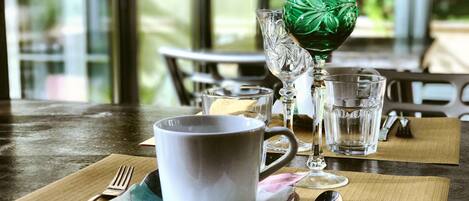 A dining table with a white mug, a green glass, and a clear glass on a placemat.