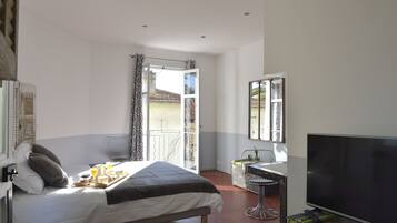 Een slaapkamer met een bed, een ontbijttafel, televisie en een balkon met uitzicht.
