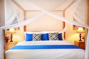 Ein Bett mit Baldachin, blaue und weiße Bettwäsche sowie zwei Nachttische mit Lampen und Blumenarrangements.