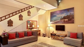 A living room with a sofa, a coffee table, a TV, a lamp, and a painting of a beach scene. - Concetta Villa Seminyak Beachside (Seminyak)