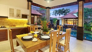 A dining area with a wooden table set for four, surrounded by wooden chairs. - Concetta Villa Seminyak Beachside (Seminyak)