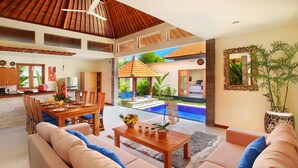 A spacious living area with a dining table, sofas, and a view of a swimming pool. - Nicola Villa Seminyak Beachside (Seminyak)