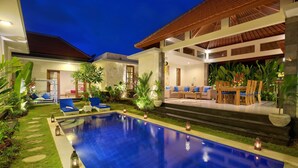 A modern poolside area with a clear blue pool, lounge chairs, and a dining area with a table and chairs. - Nicola Villa Seminyak Beachside (Seminyak)