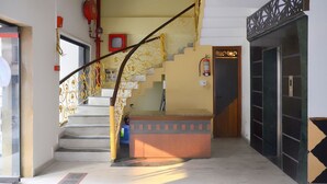 Escadaria com grades metálicas decorativas que dá para um patamar com uma pequena mesa e um extintor de incêndio na parede.
