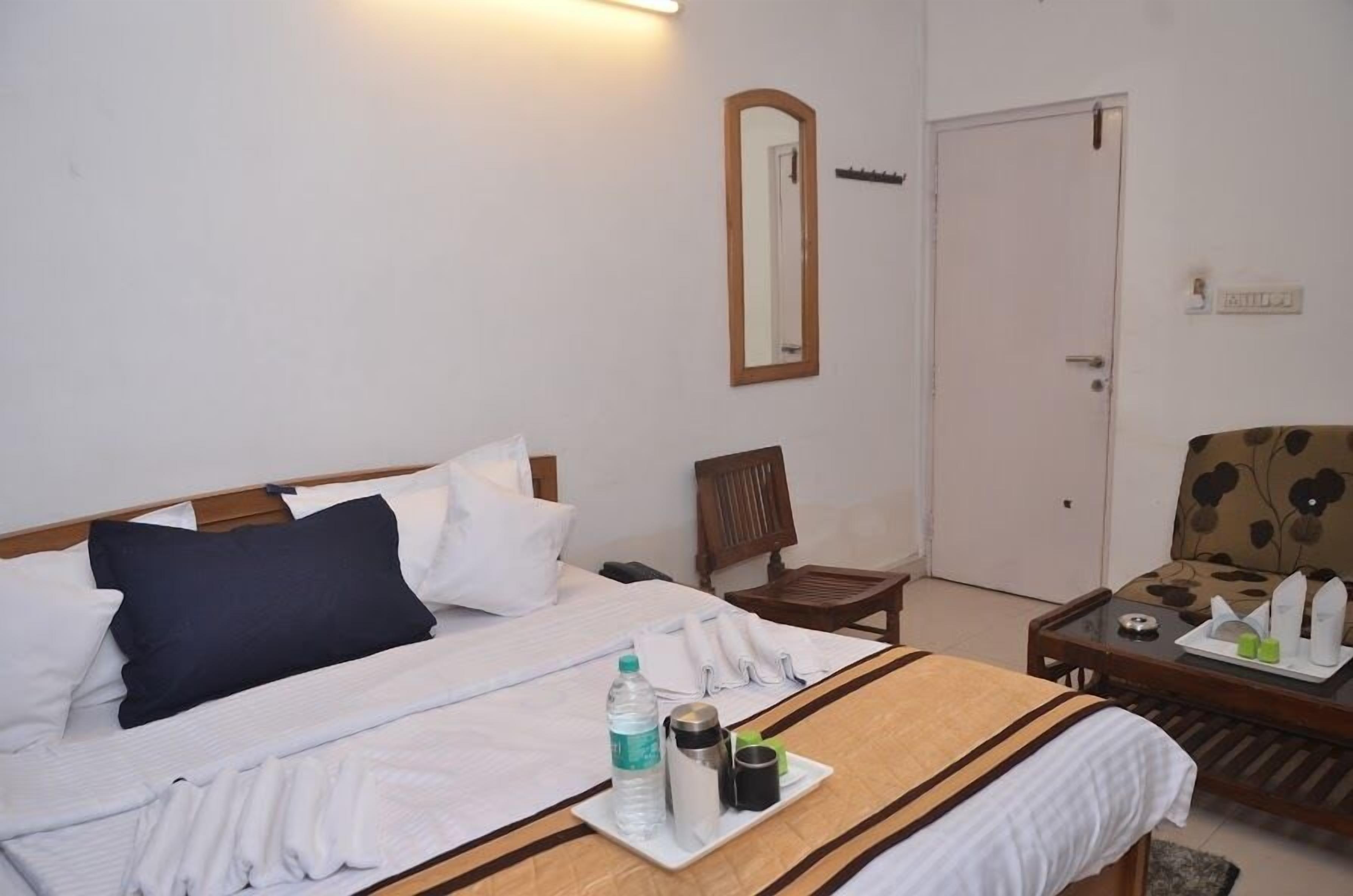 A hotel room with a bed, a chair, a small table with a tray of toiletries, and a door.