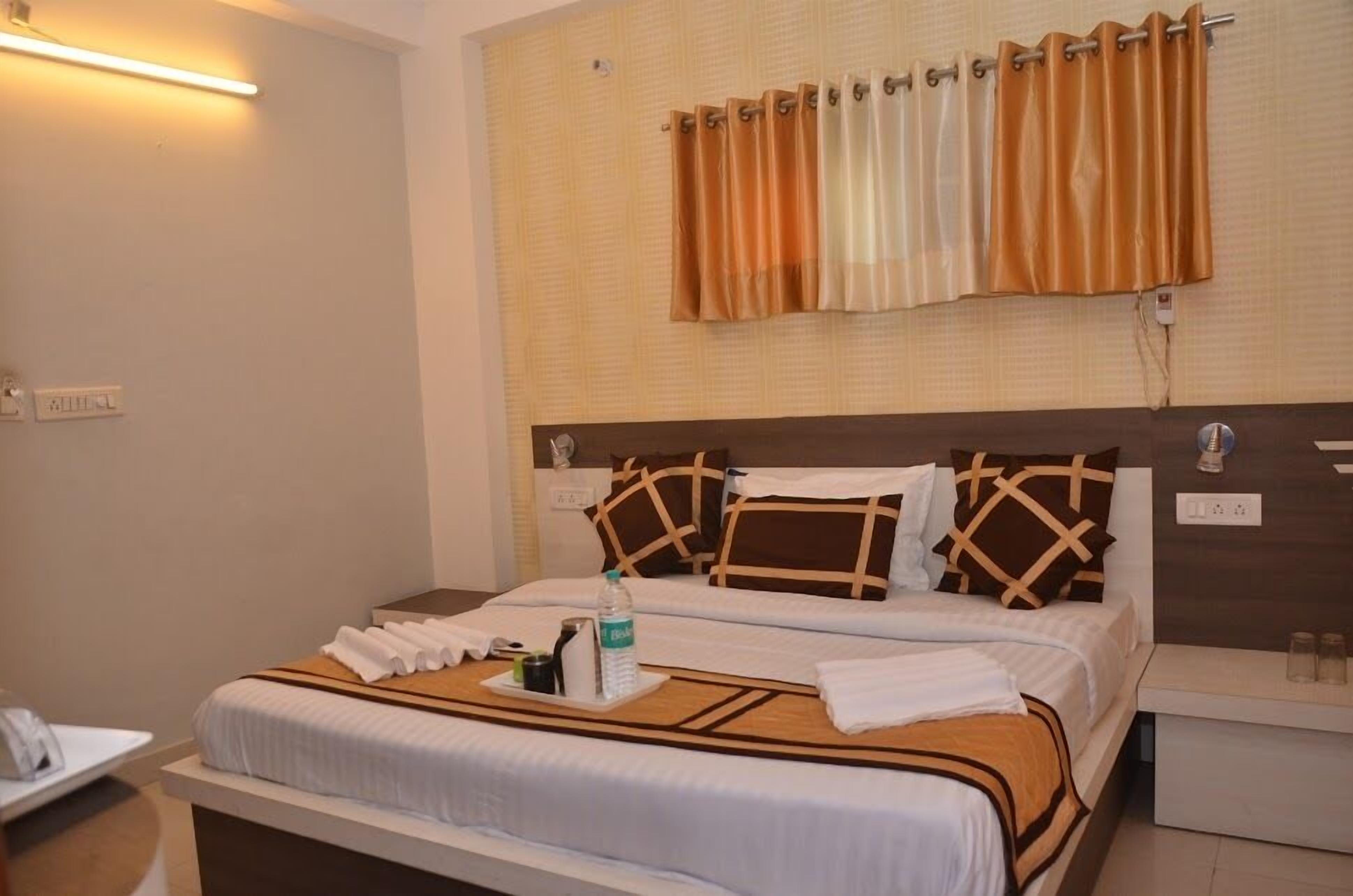 A hotel room with a large bed, a bedside table, a nightstand, and a wall-mounted curtain.