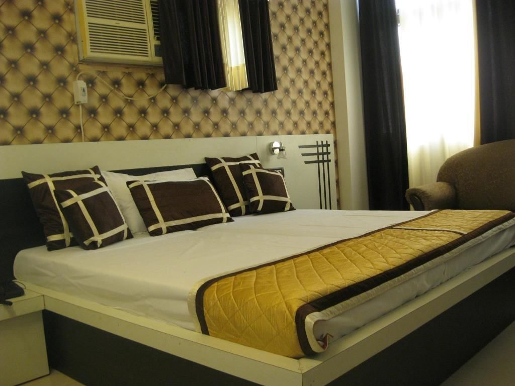 A neatly made bed with a white and yellow quilt, a headboard with a decorative pattern, and a window with curtains.