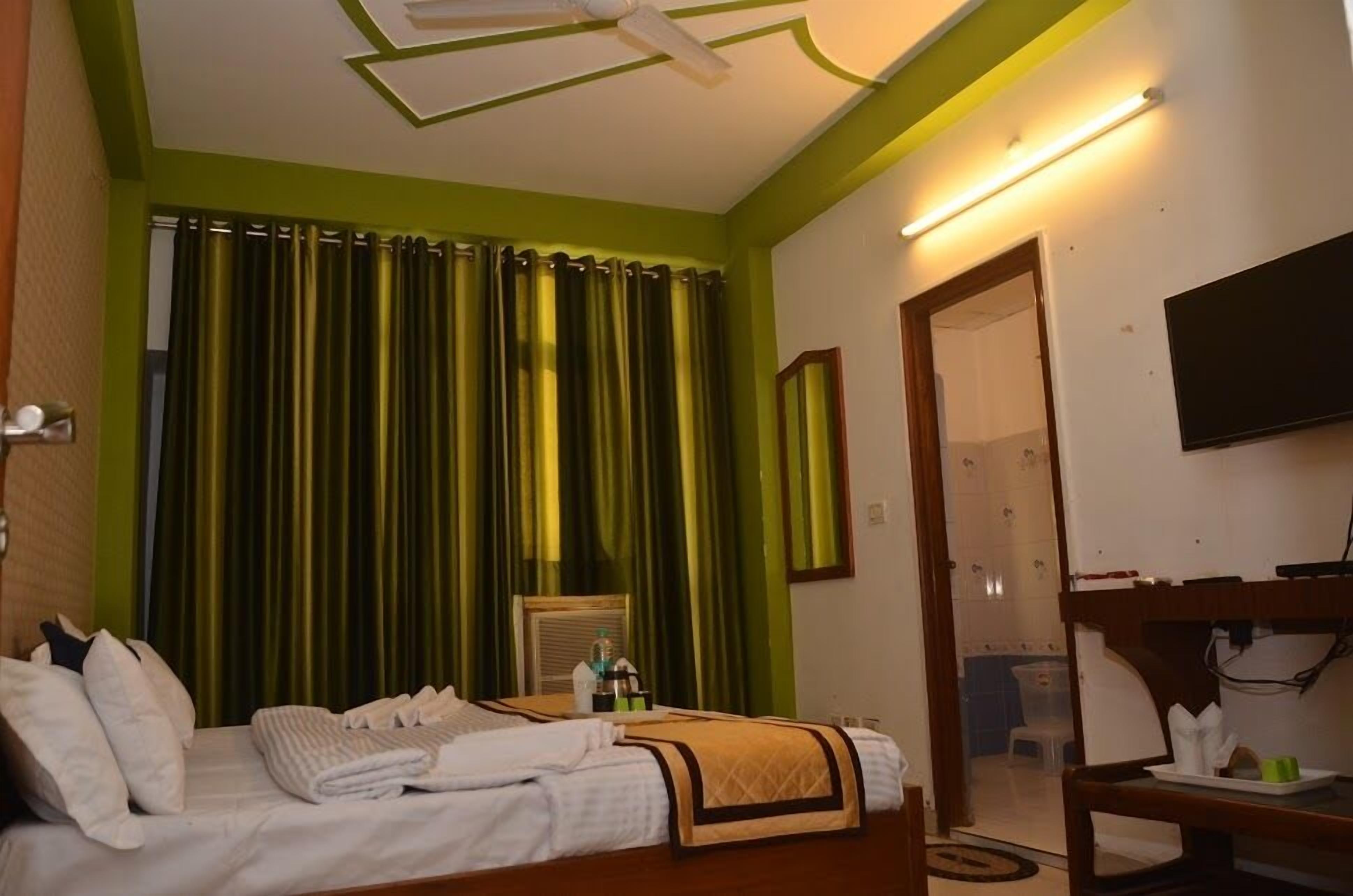 A hotel room with a bed, a desk, a chair, a flat-screen TV, and a bathroom visible through an open door.
