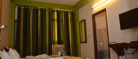 A hotel room with a bed, a desk, a chair, a flat-screen TV, and a bathroom visible through an open door.