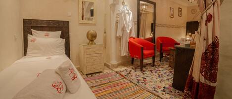 Una habitación de hotel con cama, cómoda, silla roja, espejo y alfombra colorida.