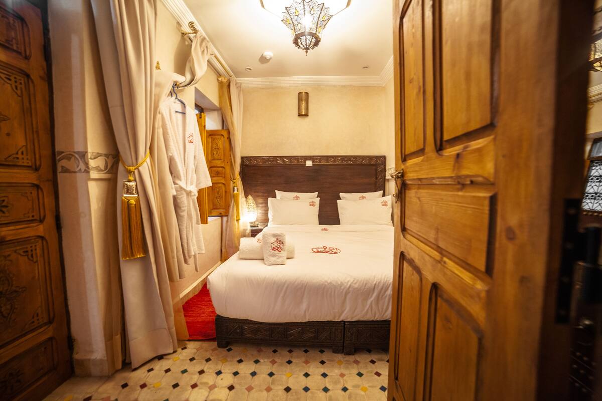 A bedroom with a wooden headboard, a bed with white linens, and a patterned floor.