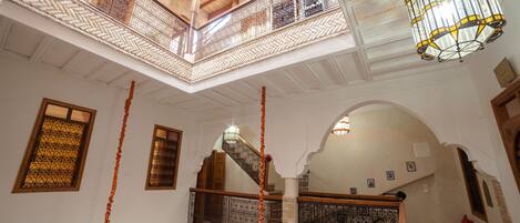 A high-ceilinged atrium with ornate metal railings, a wooden staircase, and hanging lamps.