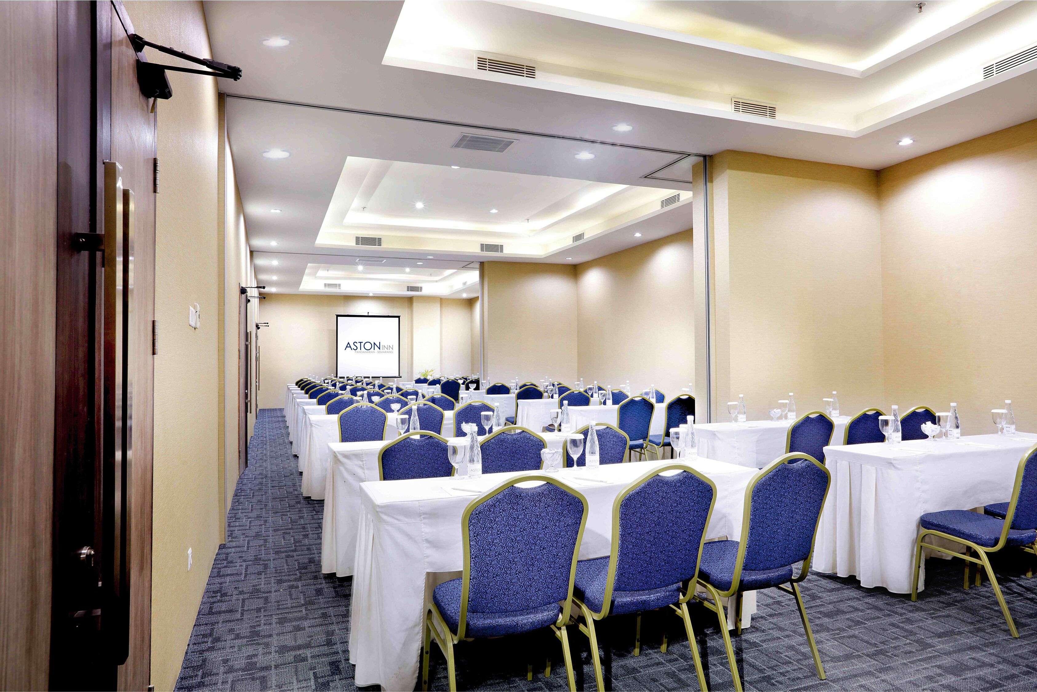 A conference room with rows of tables and chairs, equipped with water bottles and glasses.