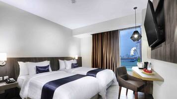 A hotel room with a large bed, a desk with a chair, a TV mounted on the wall, and a window with curtains.