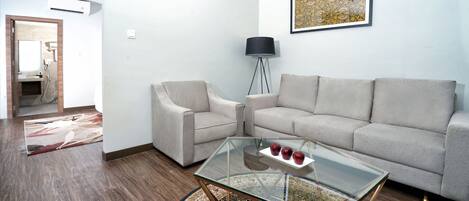 A living room with a sofa, two armchairs, a glass coffee table, and a floor lamp.