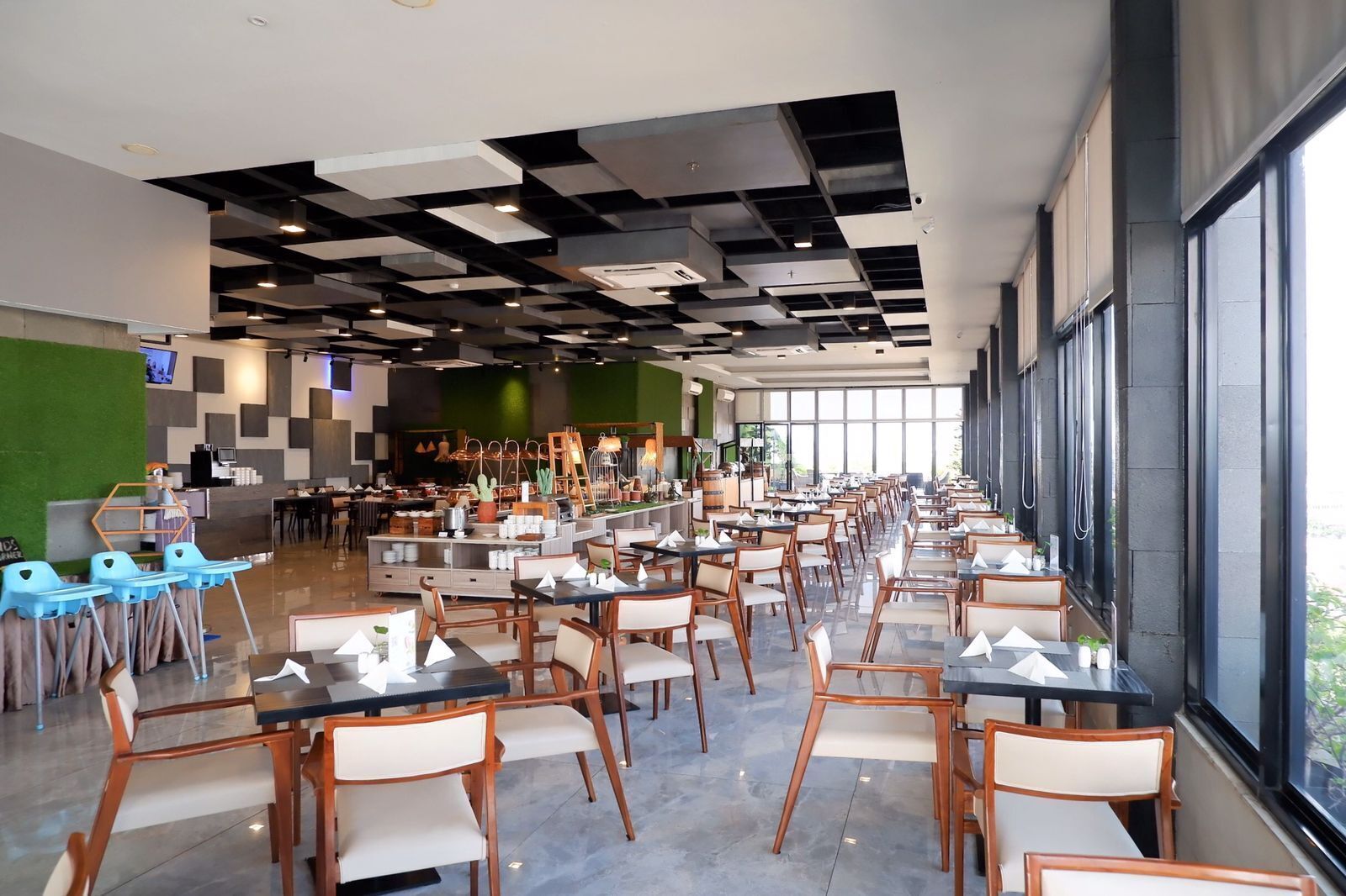 A spacious restaurant with a modern ceiling design, large windows, and a variety of seating arrangements.