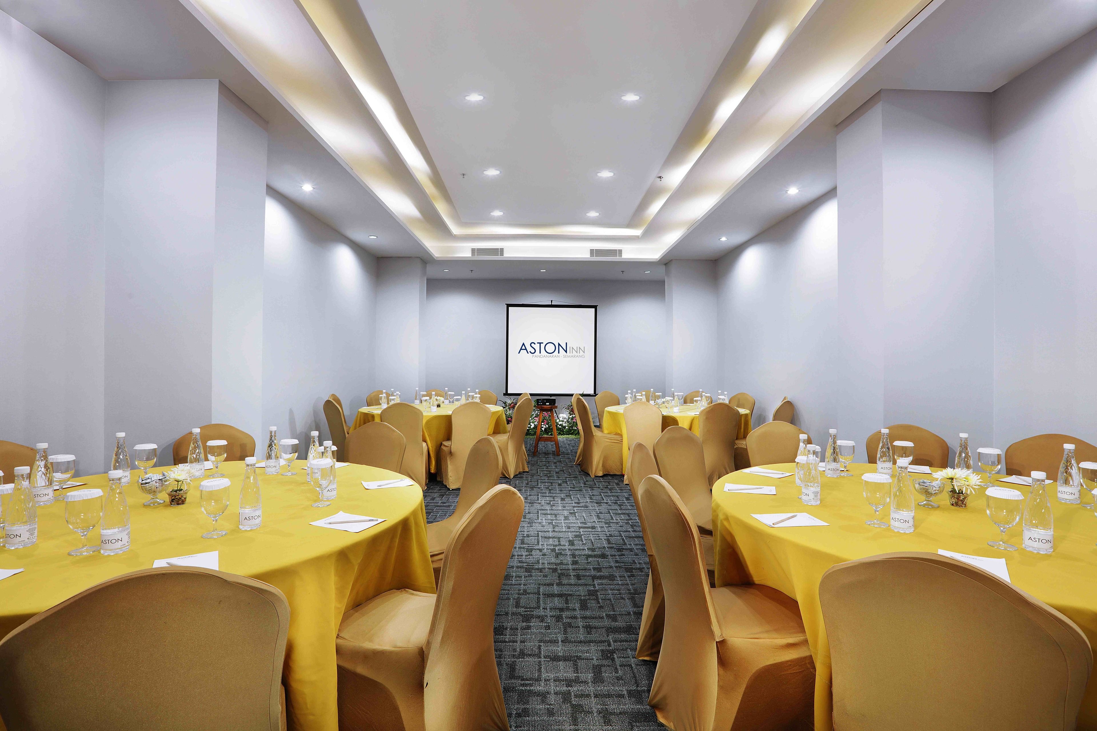 A conference room with tables set for a meeting, a projector screen, and a carpeted floor.