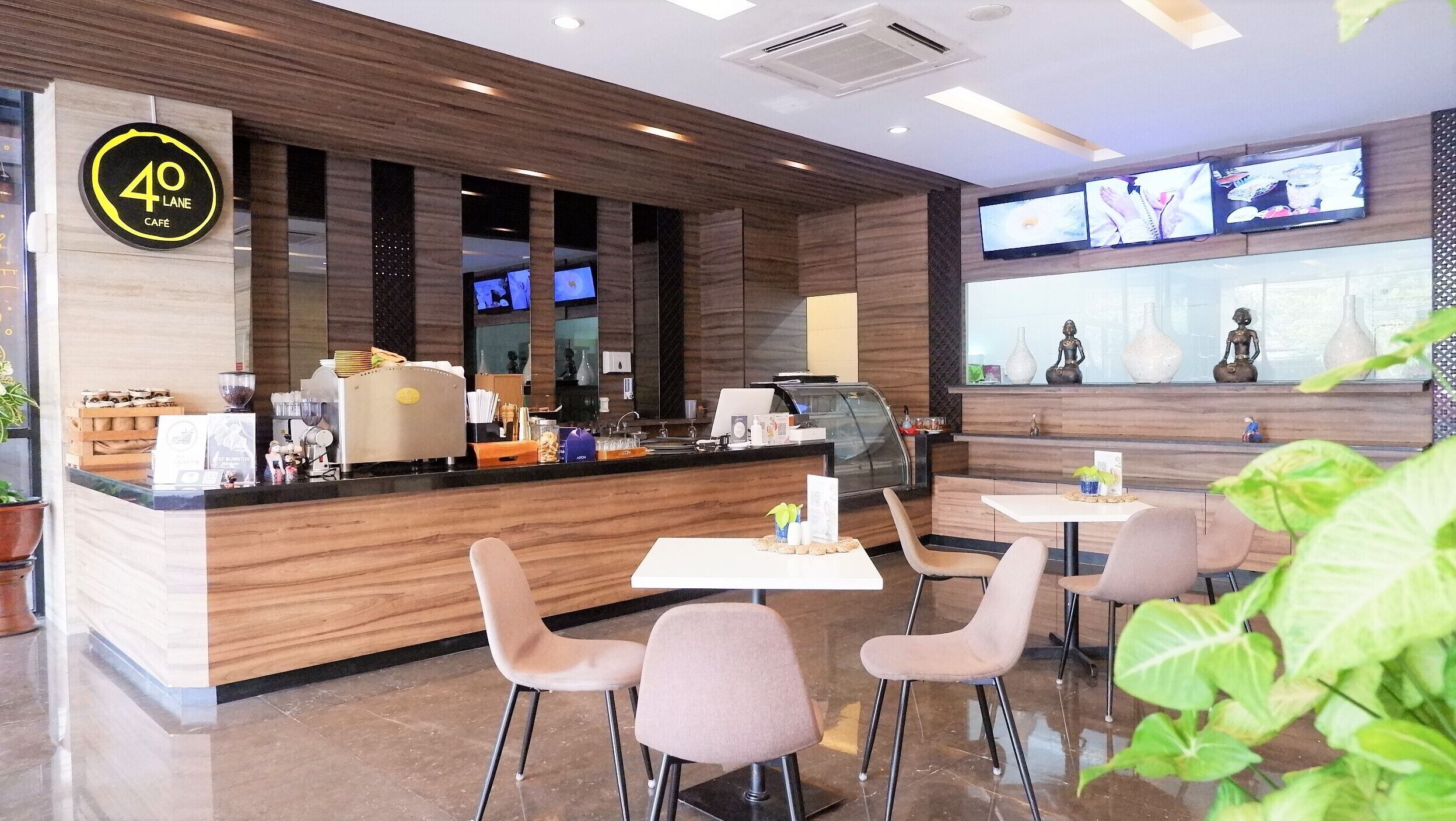 L’intérieur d’un café moderne, avec un comptoir en bois, un espace salon et des écrans numériques.