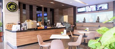 L’intérieur d’un café moderne, avec un comptoir en bois, un espace salon et des écrans numériques.