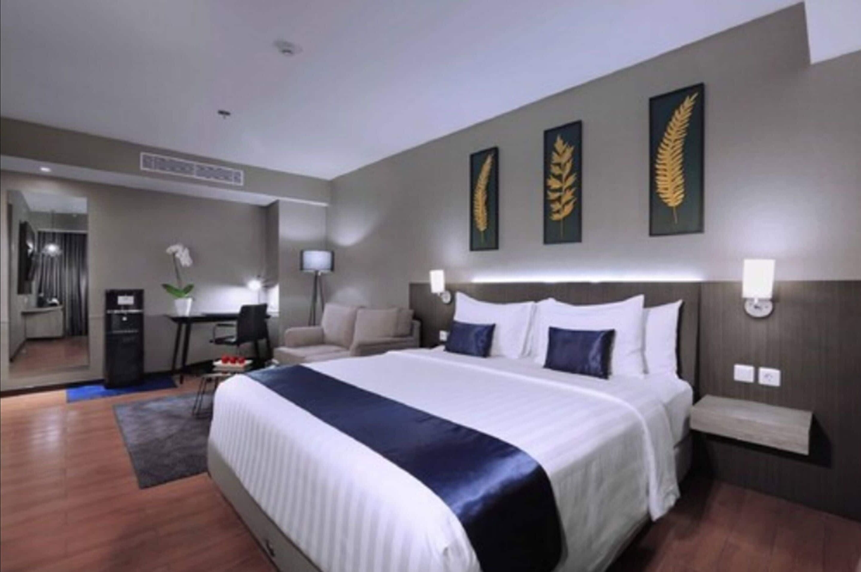 A hotel room with a large bed, a desk, a chair, a small table, and a mirror.