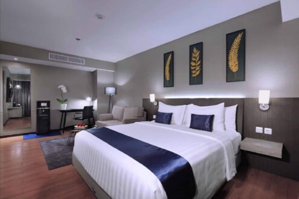Ein Hotelzimmer mit einem großen Bett, einem Schreibtisch, einem Sessel, einem kleinen Tisch und einem Spiegel.