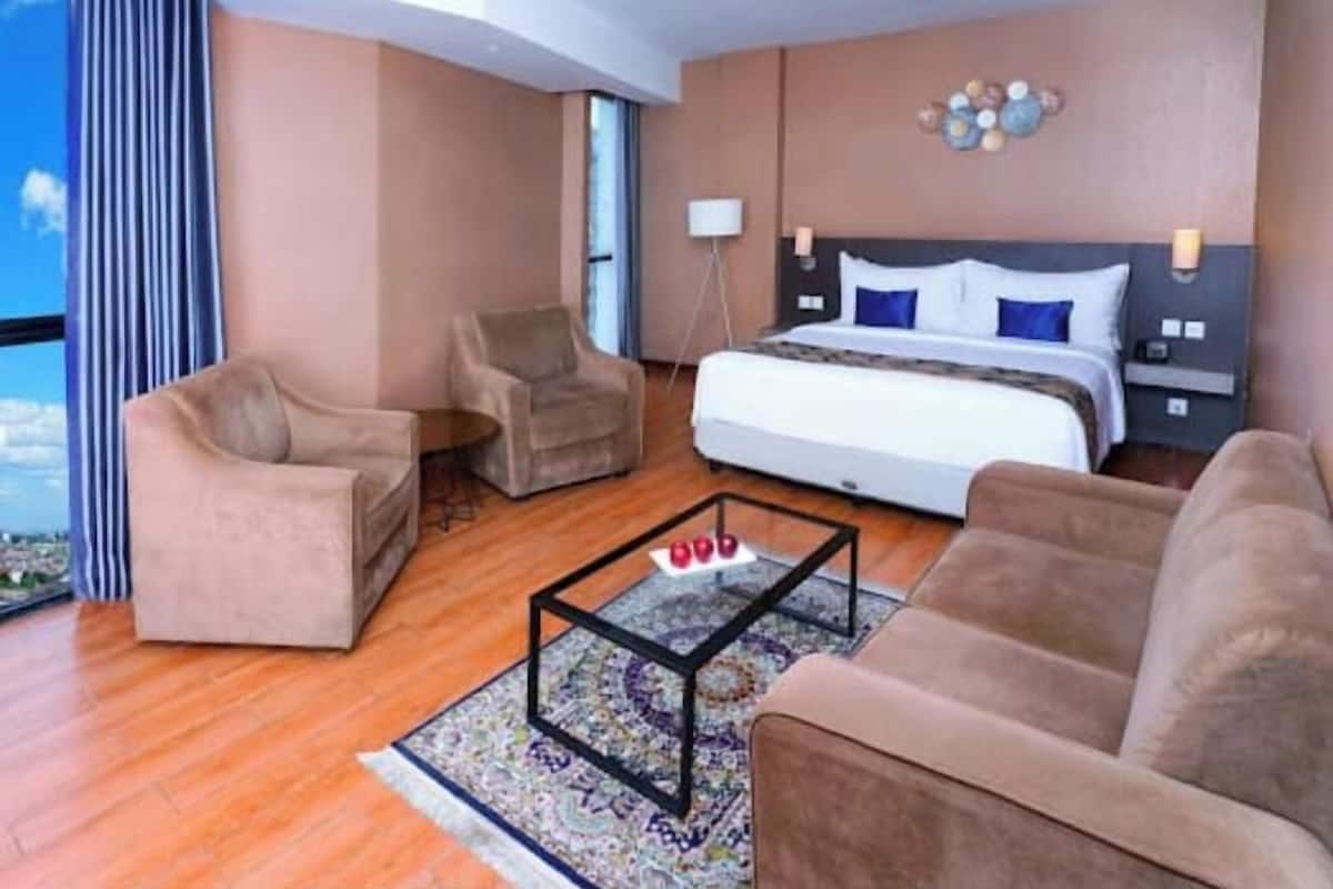 Ein Hotelzimmer mit einem Bett, zwei Sesseln, einem Couchtisch und Blick auf die Stadt.