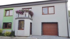 Una casa de dos pisos con fachada verde, puerta de garaje marrón y un balcón con flores.