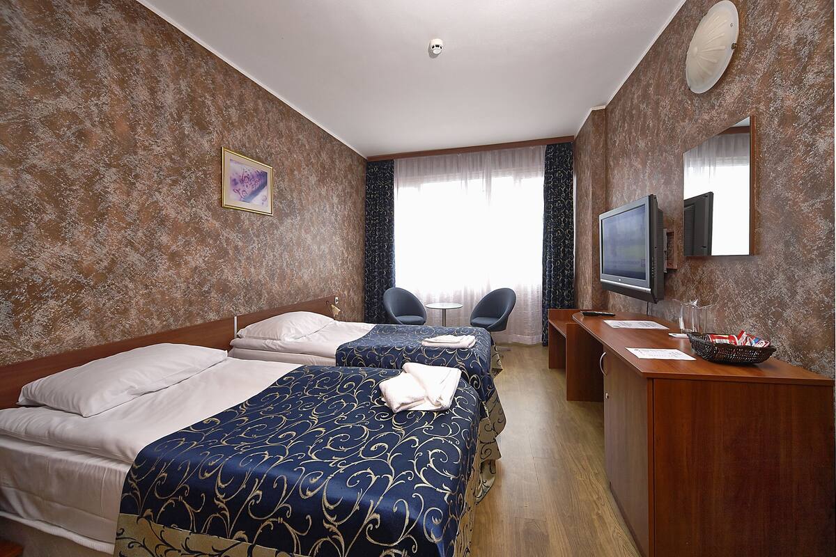 A hotel room with two beds, a desk, a TV, and a bathroom mirror.
