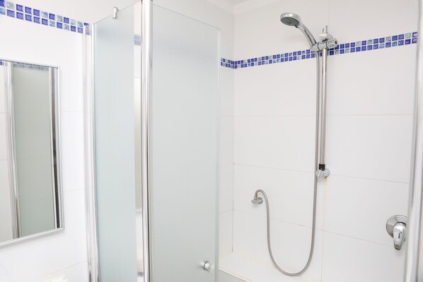 Un espace douche doté d’une porte en verre, d’un pommeau de douche à main et d’un robinet mural.