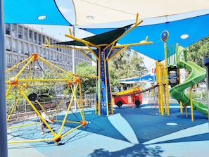 A playground with climbing structures, a slide, and a playhouse. - Carmel Apartments (Haifa)