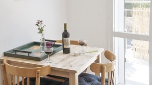 Una mesa de madera para comer con una botella de vino, dos copas, un jarrón con flores y una bandeja con un juego.