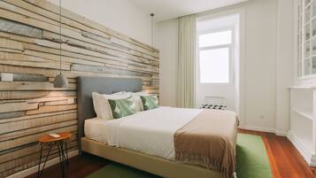 A bedroom with a wooden wall panel, a bed with white bedding, a green rug, and a window with curtains.