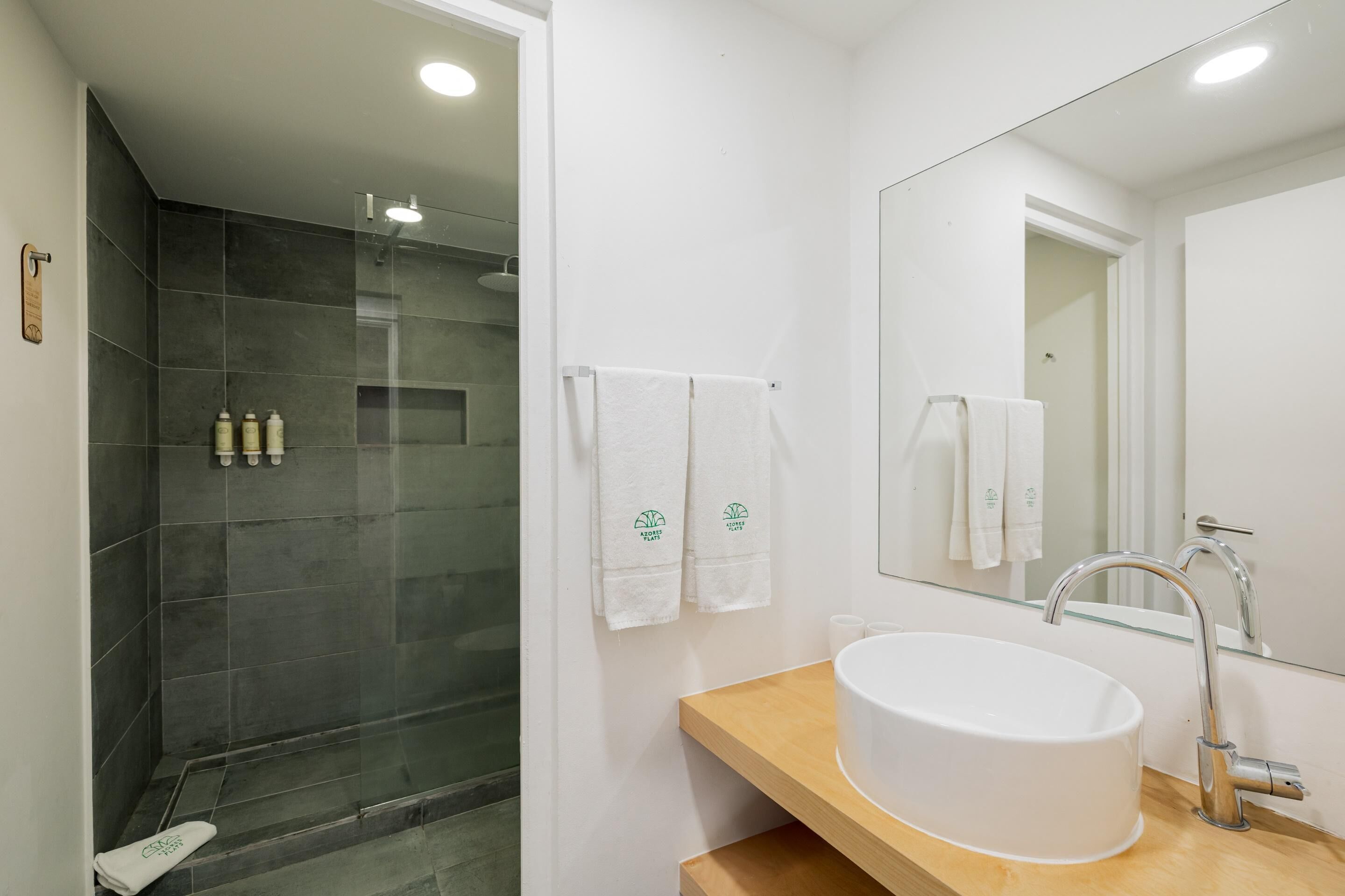 A modern bathroom with a glass-enclosed shower, a white sink with a wooden countertop, and a large mirror.