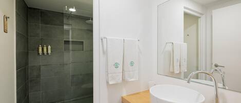 A modern bathroom with a glass-enclosed shower, a white sink with a wooden countertop, and a large mirror.