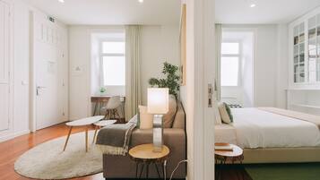 A modern hotel room with a bed, a sofa, a desk, and a lamp.