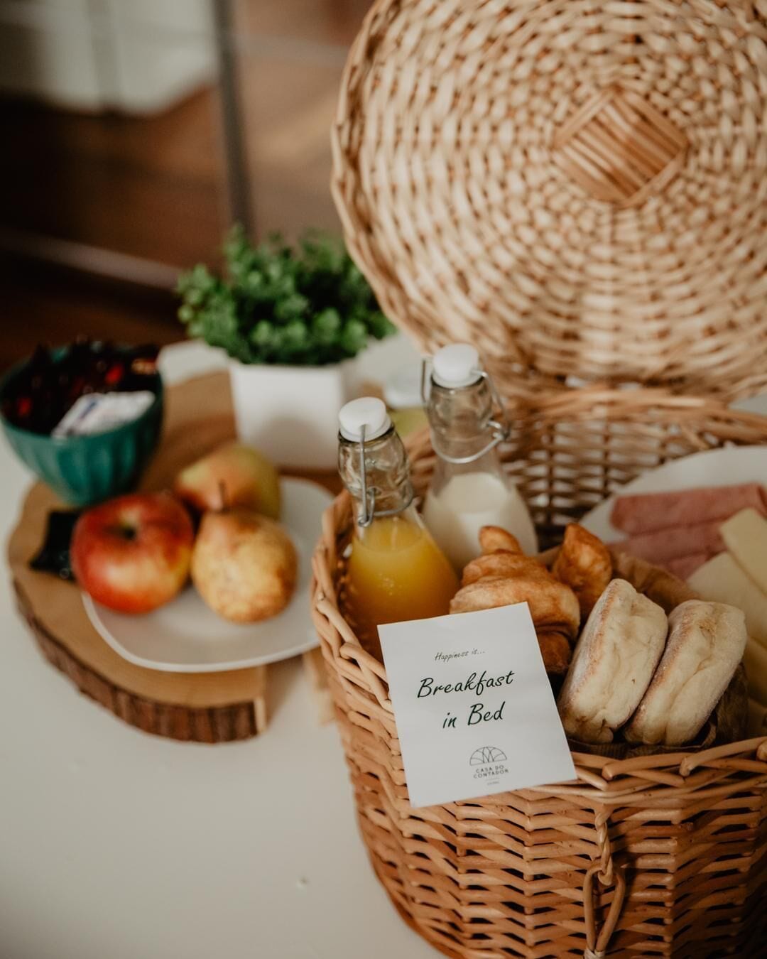 Una cesta de mimbre con artículos de desayuno, como manzanas, pan y botellas de jugo.