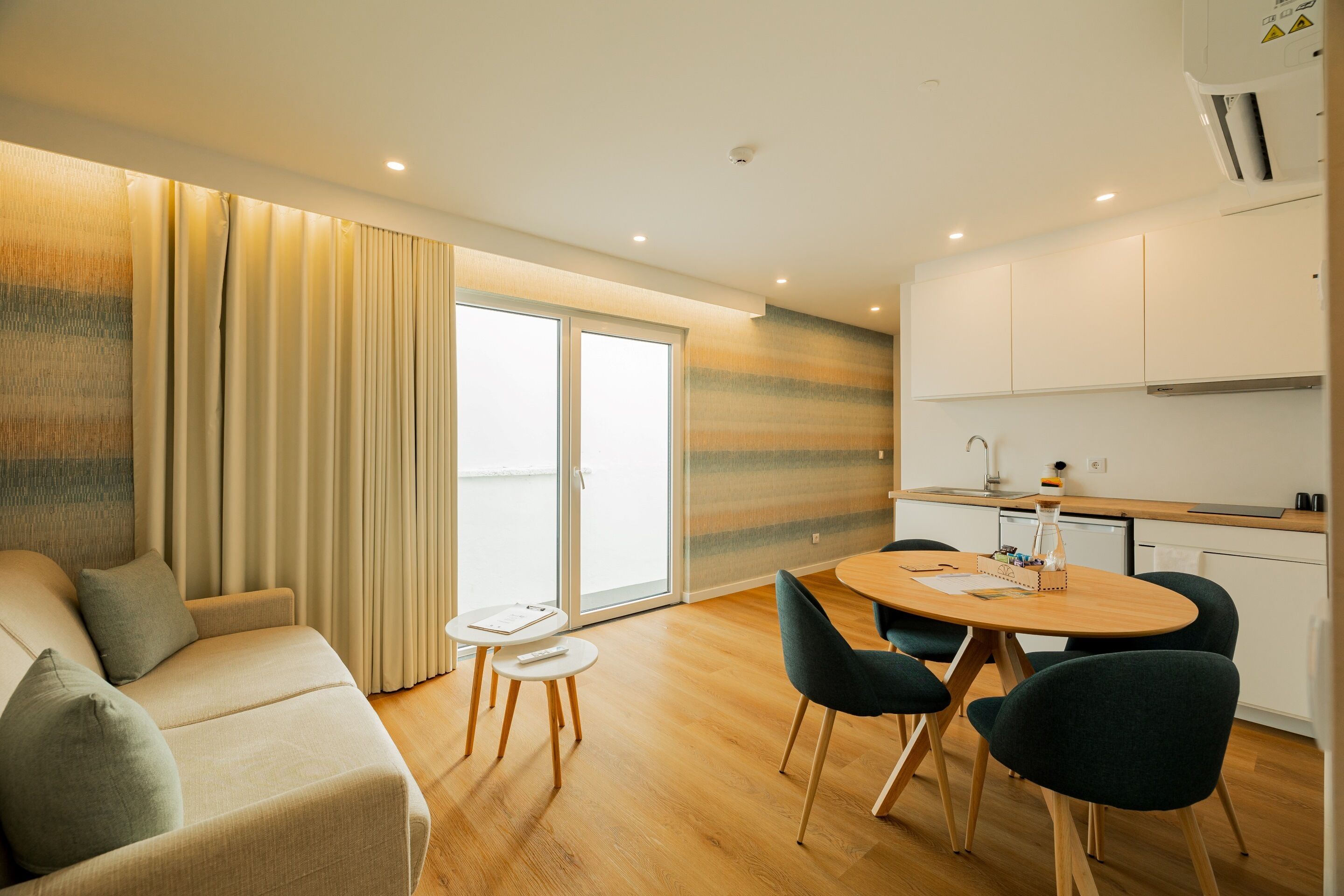 A modern living room with a sofa, a dining table with chairs, and a kitchen area with cabinets and a sink.
