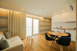 A modern living room with a sofa, a dining table with chairs, and a kitchen area with cabinets and a sink.