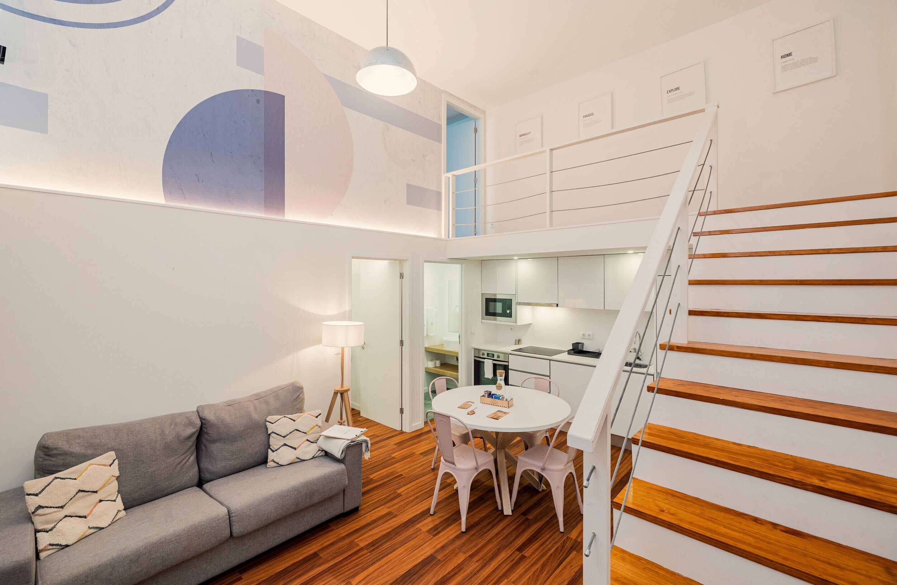 A modern living room with a grey sofa, a round table, and a staircase with wooden steps.
