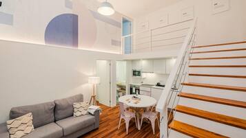Una sala moderna con un sofá gris, una mesa redonda y una escalera con escalones de madera.