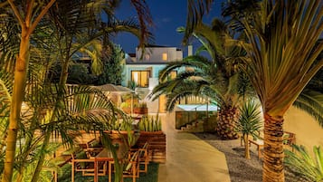 A modern house with a pool, surrounded by lush tropical plants and a well-lit outdoor seating area.