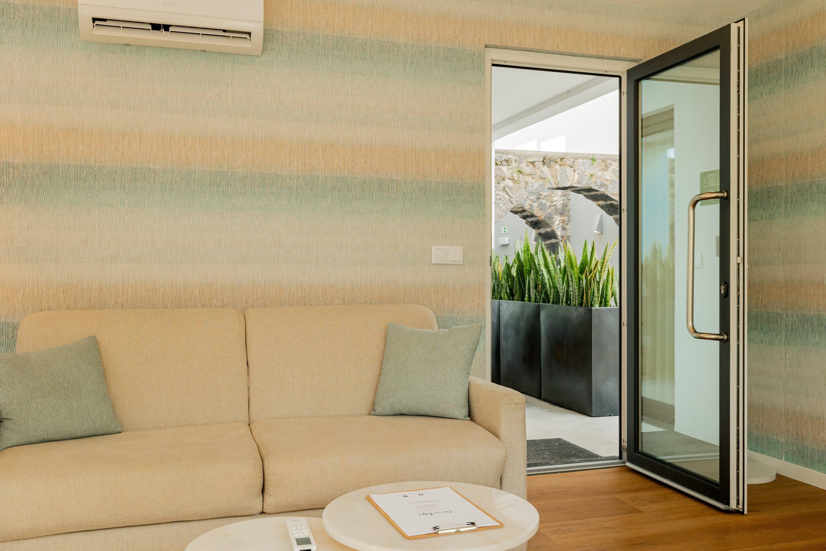 A modern room with a beige sofa, a small round table with a clipboard, and a glass door leading outside.