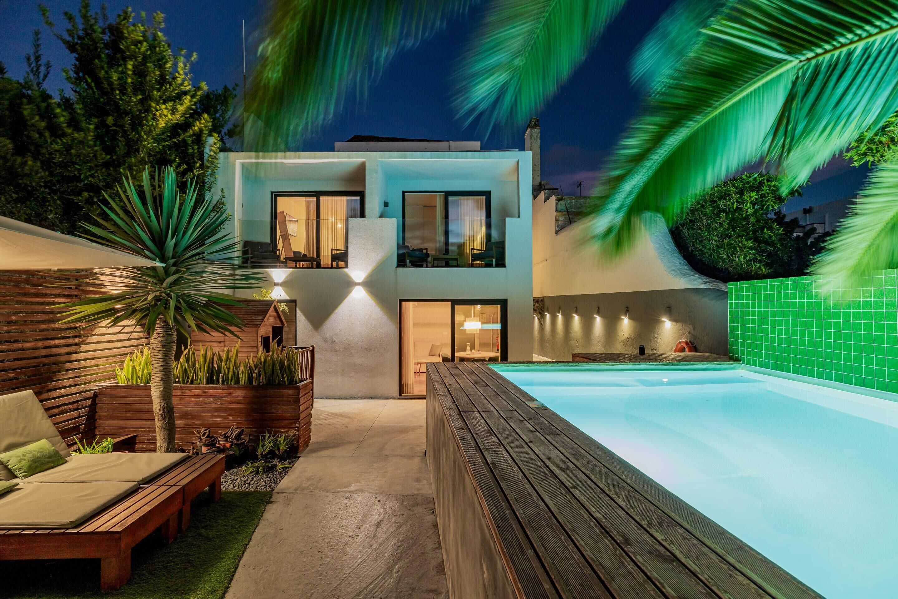 A modern two-story house with a swimming pool, wooden deck, and outdoor seating area.